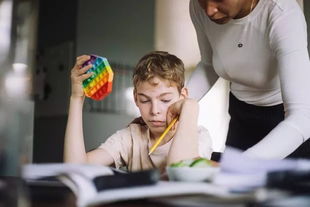 Mother-assisting-son-holding-push-pop-toy-while-doing-studies-at-home